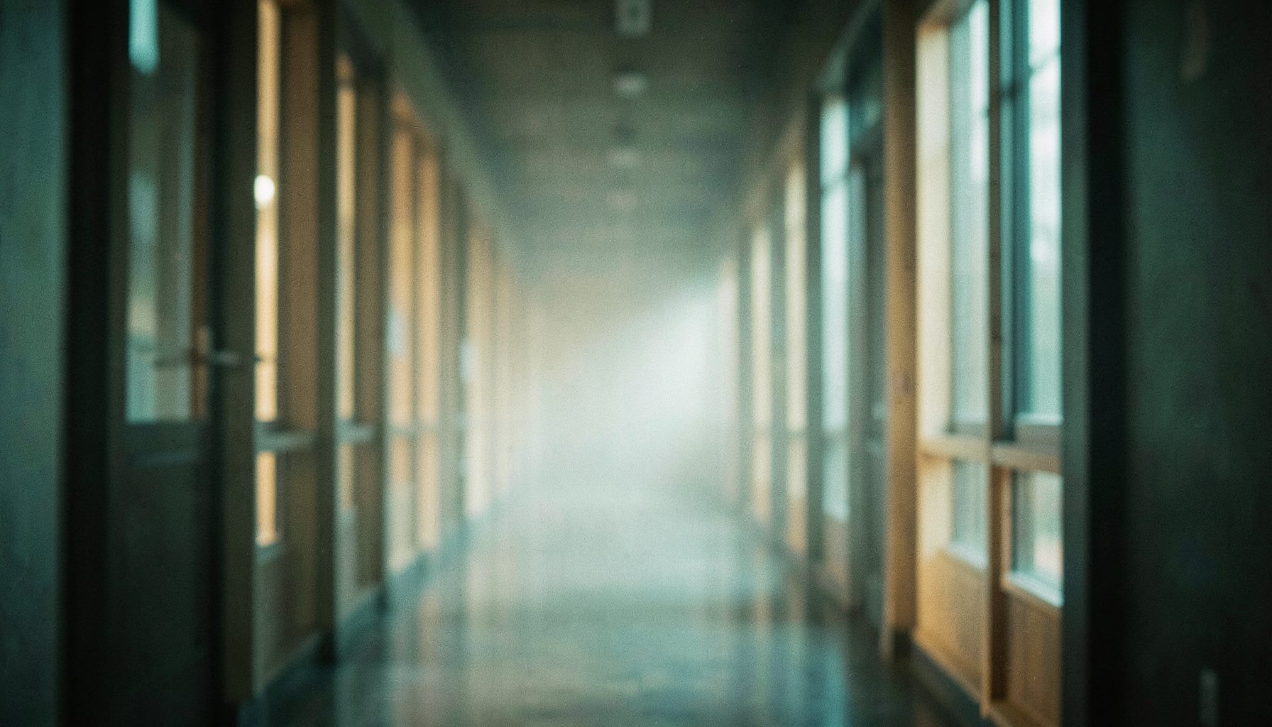 Soft focus view of a long corridor lined with tall windows, fog drifting through warm teal light.